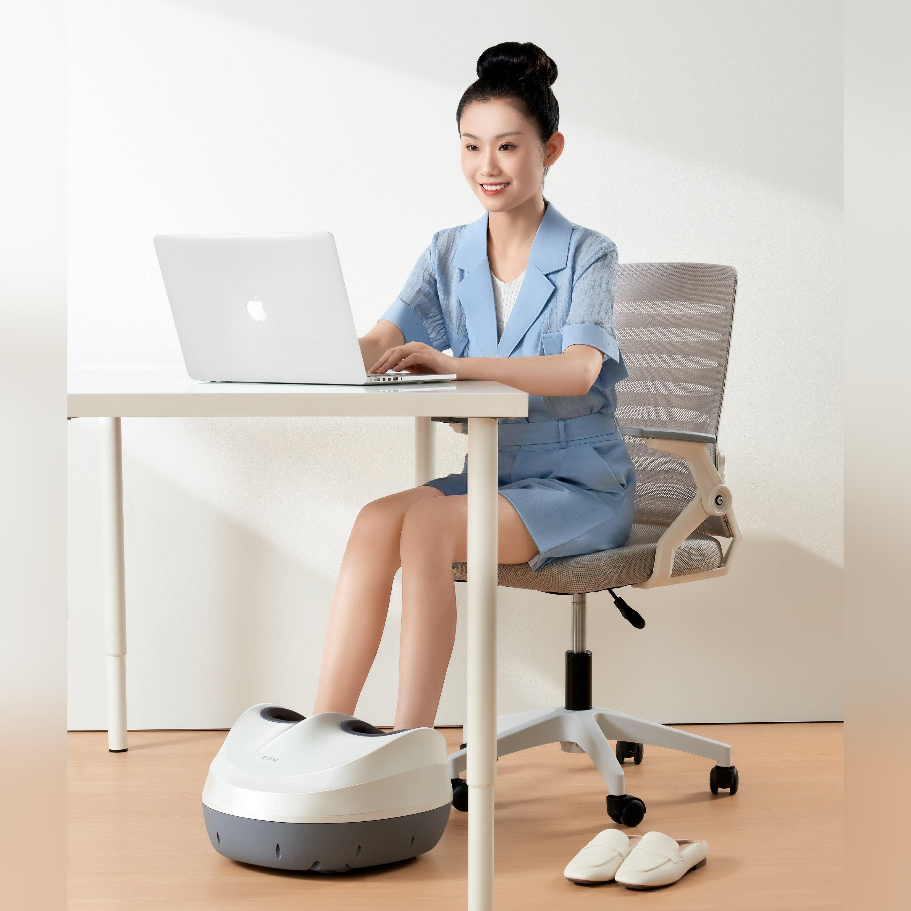 Woman using a foot massager while working at a desk in an office setting