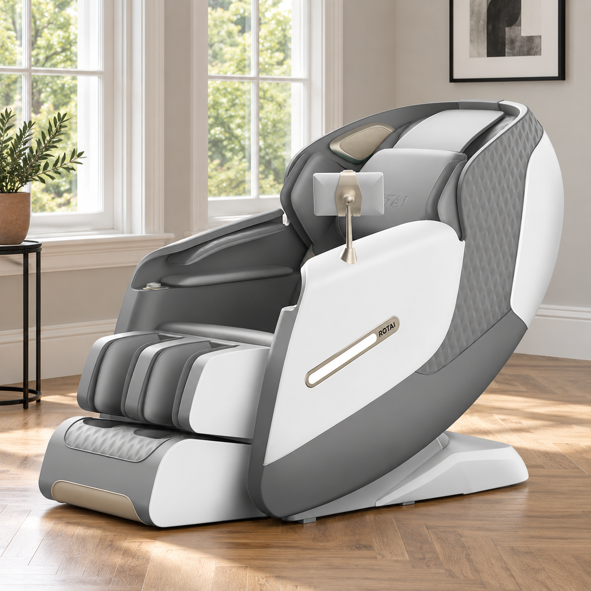 A modern white and gray automatic massage chair with a vertical armrest and a small tablet holder, set in a bright room with a wooden floor, windows, and a potted plant.