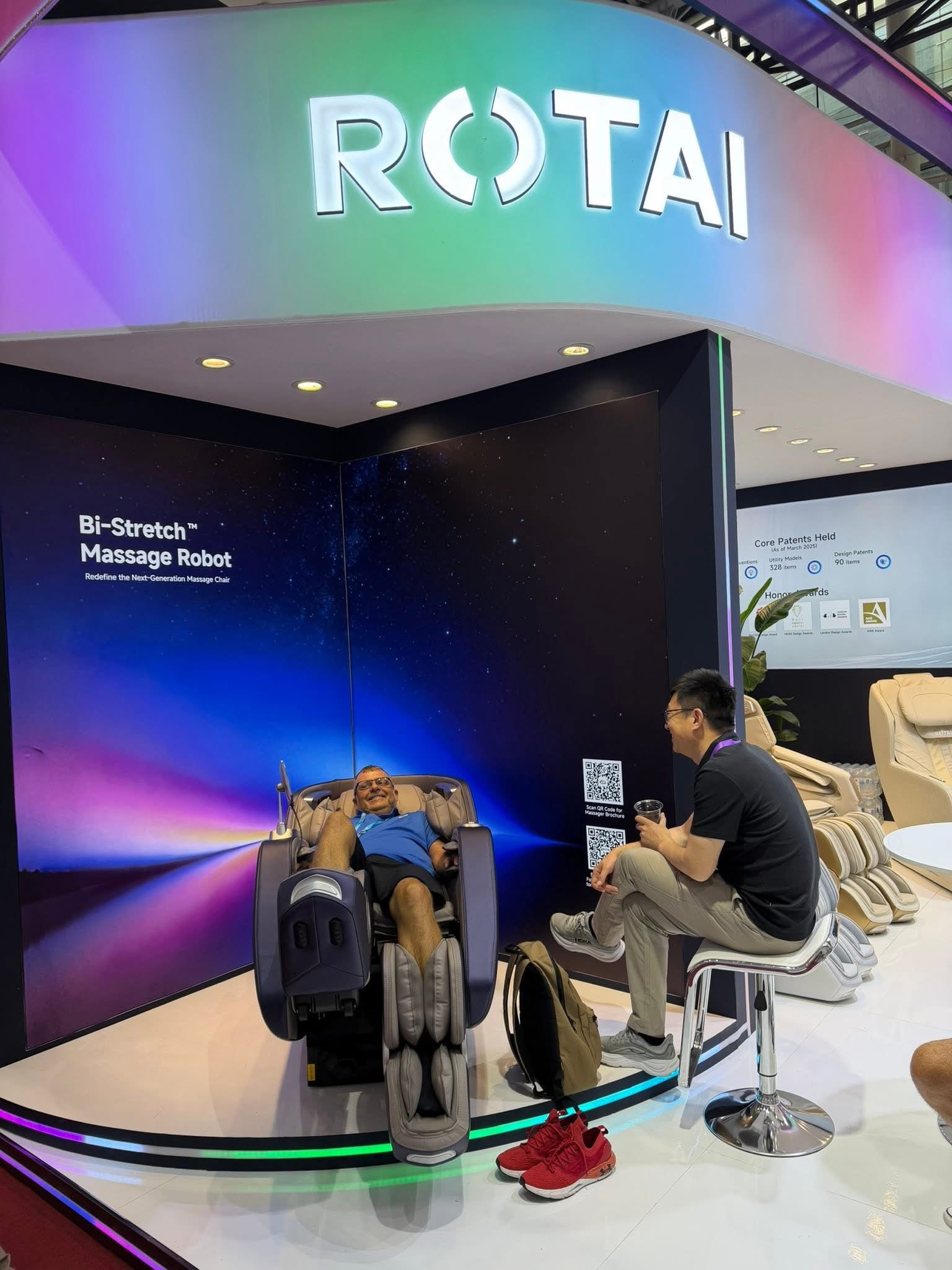 Man relaxing in a full body massage chair at an exhibition booth with modern lighting